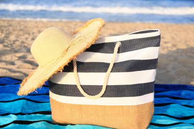 Hasır şapkalı ve kumsaldaki çantalı bir havlu.