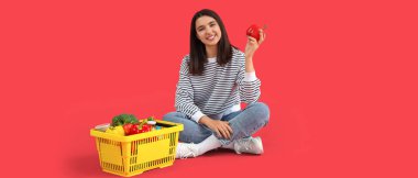 Kırmızı arka planda alışveriş sepeti olan genç bir kadın. 