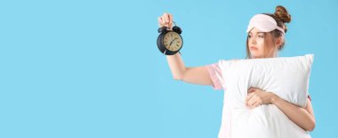 Çalar saat ve yastıklı hoşnutsuz genç kadın açık mavi arka planda ve metin için yeri var