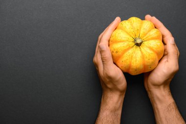 Siyah arka planda balkabağı olan erkek eller.