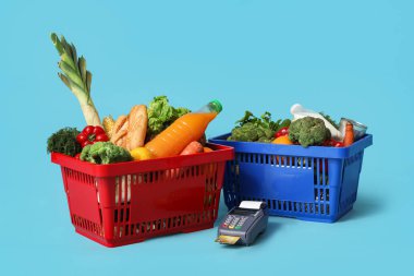 Ödeme terminali ve kredi kartıyla dolu alışveriş sepetleri mavi arka planda.