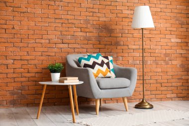 Yastıklı gri koltuk, sehpa ve kahverengi tuğla duvarın yanında standart lamba.
