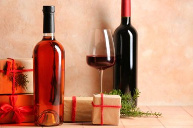 Şişe ve bir bardak şarap, üzerinde Noel hediyesi kutuları olan pembe fayanslar.