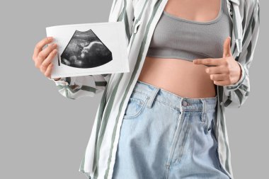 Genç hamile kadın arka planda sonogram görüntüsüne işaret ediyor, yakın plan.