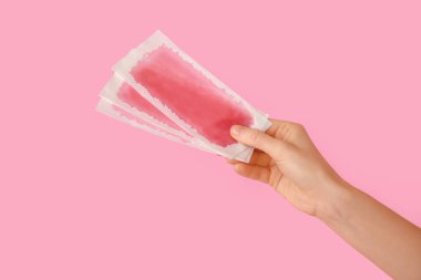 Pembe arka planda balmumu şeritli kadın eli