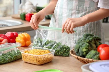 Mutfakta dondurmak için yeşil fasulyeli plastik poşet tutan kadın.