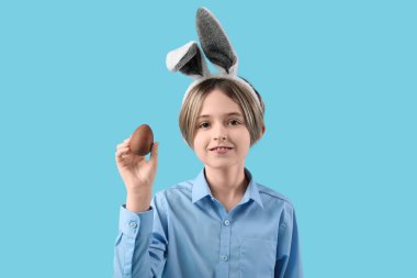 Mavi arka planda çikolatalı yumurtası olan tavşan kulaklı şirin bir çocuk. Paskalya kutlaması