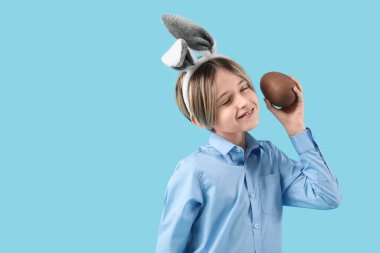 Mavi arka planda çikolatalı yumurtası olan tavşan kulaklı şirin bir çocuk. Paskalya kutlaması