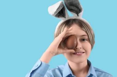 Mavi arka planda çikolatalı yumurtası olan tavşan kulaklı şirin bir çocuk. Paskalya kutlaması