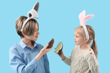 Mavi arka planda çikolata yumurtası olan tavşan kulaklı şirin çocuklar. Paskalya kutlaması