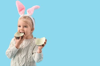 Tavşan kulaklı şirin kız mavi arka planda çikolatalı yumurta yiyor. Paskalya kutlaması