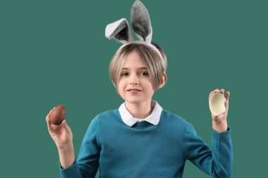 Yeşil arka planda çikolatalı yumurtası olan tavşan kulaklı şirin bir çocuk. Paskalya kutlaması