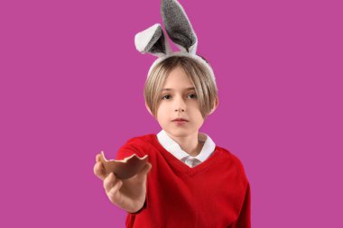 Mor arka planda çikolata yumurtası olan tavşan kulaklı şirin bir çocuk. Paskalya kutlaması