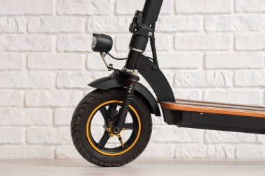 Modern elektrikli scooter beyaz tuğla duvarın yanında, yakın plan.