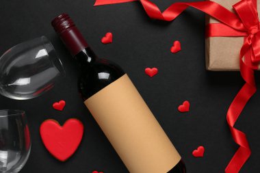 Bottle of wine, glasses, gift box and hearts on black background. Valentine's Day celebration
