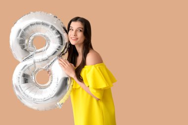 Kahverengi arka planda 8 şeklinde gümüş renkli hava balonu olan güzel genç bir kadın. Uluslararası Kadınlar Günü