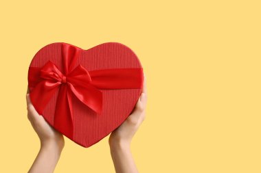 Sarı arka planda kalp şeklinde hediye kutusu olan kadın elleri. Sevgililer Günü kutlaması