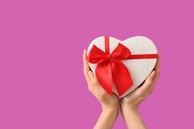 Mor arka planda kalp şeklinde hediye kutusu olan kadın elleri. Sevgililer Günü kutlaması