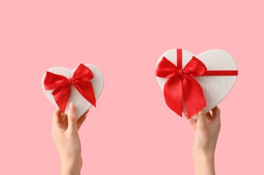 Pembe arka planda kalp şeklinde hediye kutuları olan kadın elleri. Sevgililer Günü kutlaması
