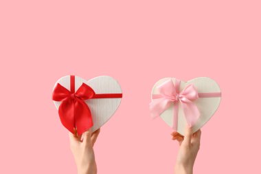 Pembe arka planda kalp şeklinde hediye kutuları olan kadın elleri. Sevgililer Günü kutlaması