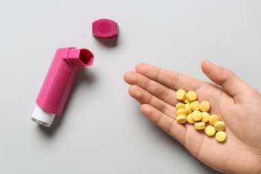 Astım spreyli bir çocuk eli ve beyaz arka planda haplar.