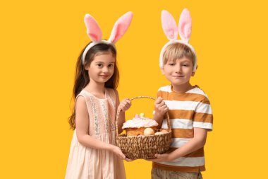 Tavşan kulaklı şirin çocuklar. Paskalya pastası sepeti ve sarı arka planda yumurtalar.