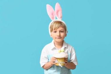 Mavi arka planda Paskalya pastası olan tavşan kulaklı şirin bir çocuk.