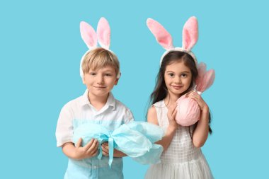 Mavi arka planda Paskalya hediyesi yumurtaları olan tavşan kulaklı şirin çocuklar.