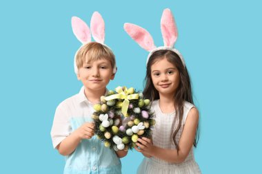 Mavi arka planda Paskalya çelengi olan tavşan kulaklı şirin çocuklar.