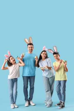 Mavi arka planda Paskalya yumurtaları olan tavşan kulaklı mutlu bir aile.