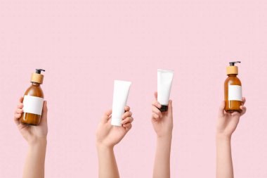 Pembe arka planda farklı kozmetik ürünleri olan kadın elleri