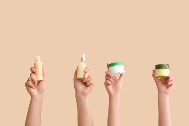 Kozmetik yağlı kadın elleri ve bej arka planda krem kavanozları.