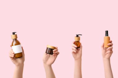 Pembe arka planda farklı kozmetik ürünleri tutan kadınlar