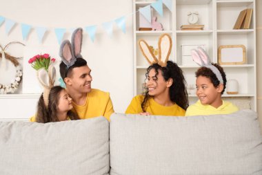 Paskalya günü evdeki kanepenin arkasında tavşan kulaklı mutlu bir aile.