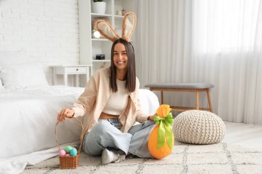 Tavşan kulaklı ve paskalya yumurtalı genç bir kadın yatak odasında oturuyor.