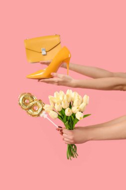 Bir buket lale, yüksek topuklu ayakkabı ve pembe arka planda el çantası olan kadın elleri. Uluslararası Kadınlar Günü için Alışveriş