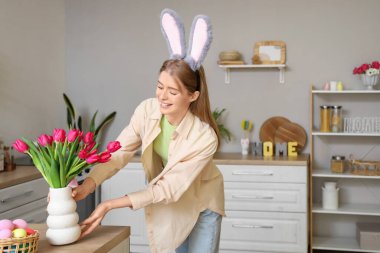 Paskalya yumurtaları ve laleleri evdeki mutfak masasında duran tavşan kulaklı genç bir kadın.
