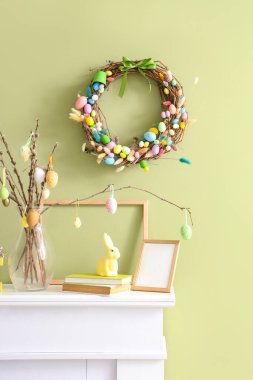 Dekorlu şömine rafı ve yeşil duvarlı Paskalya çelengi.