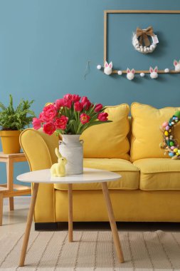 Vase with tulips and Easter rabbit on table in living room