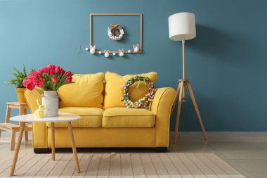 Paskalya çelenkleri, kanepesi ve masası olan bir oturma odası.