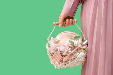 Yeşil arka planda kozmetik ürünleri olan Paskalya sepeti tutan genç bir kadın.