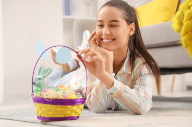 Paskalya yumurtası dolu sepeti olan genç bir kadın evde yerde yatıyor.