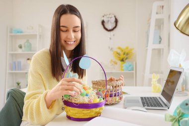 Evde elinde Paskalya yumurtası sepetleri olan genç bir kadın var.