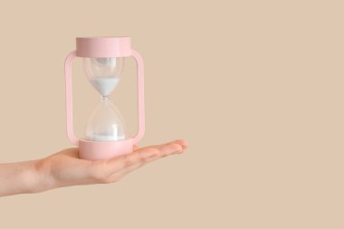 Bej arka planda kum saati tutan kadın.