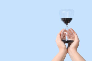 Mavi arka planda kum saati tutan kadın eller.