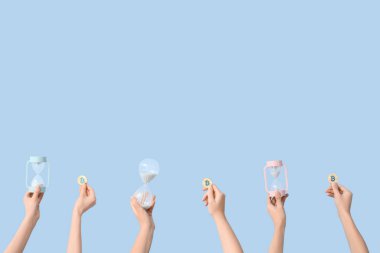 Mavi arka planda kum saati ve bitcoin tutan kadın elleri