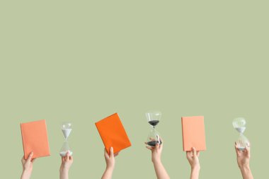 Kum saati tutan kadın eller ve yeşil arkaplan üzerine kitaplar