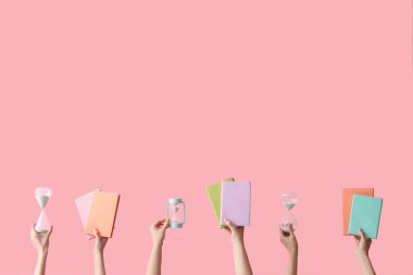 Kum saati tutan kadın eller ve pembe arka planda kitaplar.