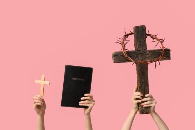 Ahşap haçlı kadın eller, kutsal İncil ve pembe arka planda dikenli taç. İyi Cuma konsepti