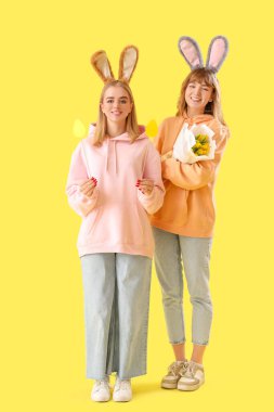 Paskalya tavşanı kulaklı genç kızlar, sarı arka planda çiçekler ve dekor.